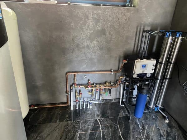 Copper and stainless steel water filtration system with multi-stage filters and pressure gauges in a modern indoor setting.
