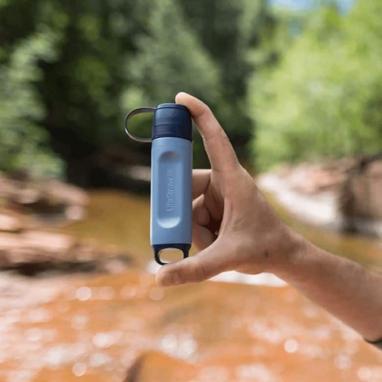 Small portable water filter device held up in outdoor natural setting.